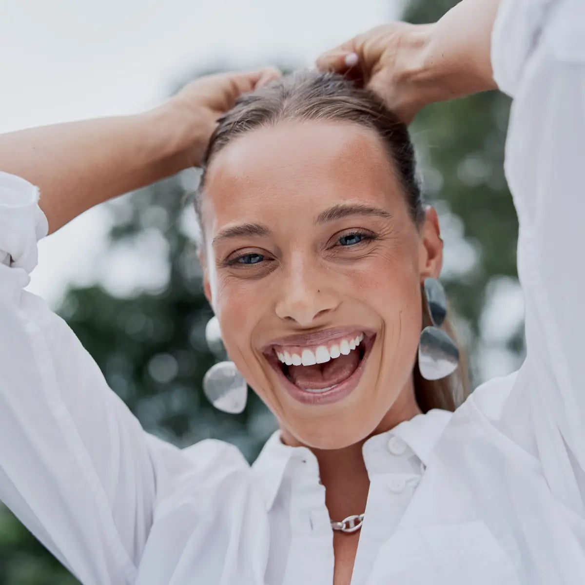 A woman smiling while adjusting her ponytail